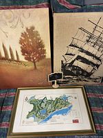 Three art pieces: two canvas paintings and one framed golf course map print, laid out against striped fabric.