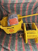 Photo of Rubbermaid Brute yellow mop bucket with attached wringer and mop with handle and mop head wrapped in plastic inside the bucket.