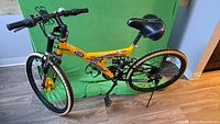 Yellow 21-speed mountain bike with front suspension fork and rear suspension. Black seat with red and white designs. Mounted gear shifters on handlebars and kickstand attached to rear frame. Tires show some signs of use but tread is visible.