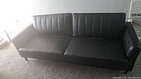 Front angle of black faux leather couch with both backrests upright showing channel stitched vertical lines.