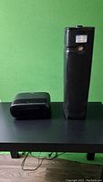 Photo of two black air purifiers on a black table against a green wall, one taller Holmes unit and one smaller 3M Filtrete unit.