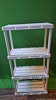 White plastic 4-tier storage rack against a green backdrop, showing all shelves and support columns.