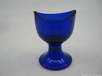 Front and side views of the cobalt blue glass eye wash cup, showing its shape, color, and air bubble details