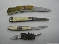 Four vintage cutting tools arranged together on a light surface including three folding knives and one train-shaped keychain knife.