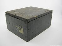 View of rectangular wooden military box closed, showing dark worn paint and dovetail joint corners.
