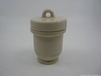 Front view of the cream-colored glazed stoneware egg coddler with lid and loop handle.