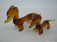 Two amber and brown glass dachshund dog figurines displayed on a white background. The larger figurine measures about 3 3/4 inches long.