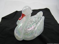 Clear glass swan paperweight with iridescent effect and marbled white/gray interior, red-orange beak, polished surface.