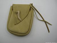 Front view of the handmade leather belt pouch showing flap closure with attached leather thong and decorative tooth/claw accent with fringes.
