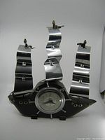 Full view of the clock showing wooden hull base, metal curved sails, and the clock face embedded at center.