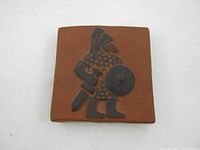 Front view of the square ceramic tile with raised Viking figure in black matte finish on terracotta background.