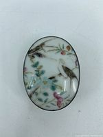 Close-up top view of the oval hand-painted porcelain lid showing birds and flowers.