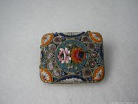 Front view of the old Italian micro mosaic brooch showing floral mosaic design with orange corner accents and detailed border mosaic work in blue, white, purple and green.