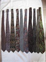 Top view of ten men's vintage ties laid out horizontally on white fabric, showing varied colors and patterns