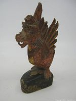 Front angled view of the wooden Balinese dragon carving showing detailed wing and head features with red and yellow paint.