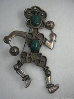 Front view of the vintage sterling silver Mexican brooch showing the dancing figure design with green stones and silver detailing.
