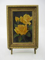 Full view of the framed flower painting with yellow roses and gold frame standing on a small easel.