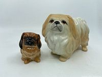Two Pekinese dog figurines side by side showing size difference and color details.