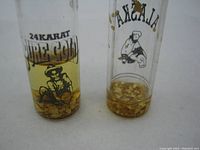 Front view of two glass vials containing gold flakes with printed labels showing 24 karat gold and Alaskan themes.