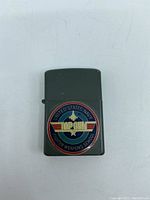 Front side of the lighter showing the United States Navy Fighter Weapons School Top Gun emblem with star and wings design on green finish.
