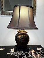 Front view of the antique-style lamp showing the fabric shade lit from the inside, and the black base with gold floral and symbolic patterns.