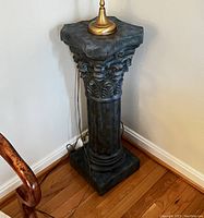 Side view of antique style pedestal column next to chair, showing its dark finish and ornate Corinthian capital
