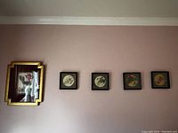 Four framed Asian paintings on a wall, including one large gold framed lotus and duck painting and three smaller black framed koi fish paintings.
