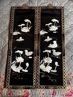 Two tall rectangular black lacquered panels with gold geometric borders and intricate mother of pearl inlay depicting ducks and lotus flowers.