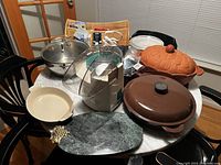 Overview of assorted pots and kitchen accessories placed on a round table in a kitchen.