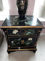 Front view of nightstand showing lotus flower and leaf design on drawer and cabinet doors with brass hardware.