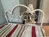 Close-up view of the full size bed's decorative white metal frame headboard with curved scrollwork and floral embossing, including a brass center rod.