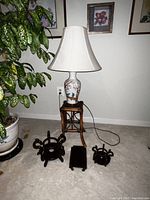 Full view of oriental ceramic lamp with fabric shade on wooden stand, plus three wooden pedestals in front on carpet.