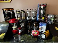 Full spread photo showing multiple camping lanterns and flashlights of various brands and styles in different colors and sizes on a black surface.