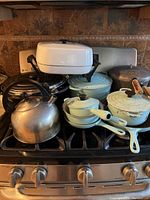Overhead view of cookware arranged on stovetop including Le Creuset seafoam green items and mismatched pieces