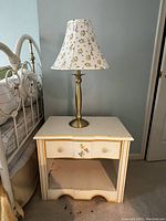 Nightstand with a floral accent drawer and brass lamp on top, showing overall appearance and size.