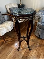 Full view of round marble top plant stand showing green veined marble top and ornate wooden legs with gold detailing