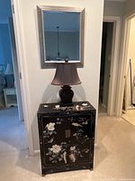Mirror hanging above a black floral cabinet with lamp, providing context for the mirror's size and style.