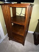 Photo of a wooden TV stand with a rotating top and three shelves, showing the vertical groove detailing on the sides and power cables behind it.