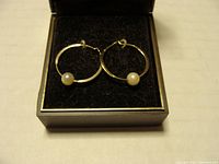 Pair of gold hoop earrings with single white cultured pearls, displayed in jewelry box.