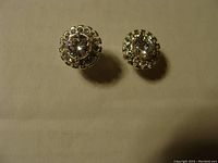 Pair of clear rhinestone stud earrings with removable bezels, rhodium finish, photographed on neutral background showing light reflections.