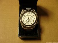 Front view of Michael Kors silver tone watch with rhinestone bezel inside a black watch box.