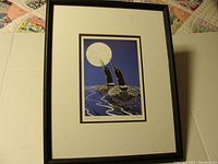 Photo of the framed print showing two loons under a full moon on water, set against a blue background