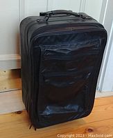 Front side view of black Bugatti genuine leather trolley bag standing upright showing front zippered pocket and handle