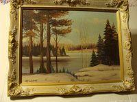 Full view of the framed landscape oil painting depicting a snowy wooded area with a lake or river, signed by the artist.
