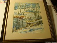 Frontal photo showing full view of the framed watercolor painting depicting a winter landscape with trees, snow, and a pond or stream.