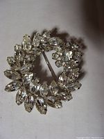 Front view of the brooch showing clear rhinestones set in silver-tone metal in a circular wreath arrangement.