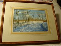 Framed watercolor artwork showing 'Road to Buck Lake' winter scene with snow and trees.
