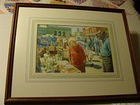 Framed watercolor painting showing an outdoor antique market scene with people browsing antiques.