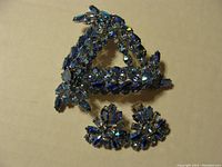 Full view of the triangular brooch set with multiple blue rhinestones and the pair of clip-on floral style earrings with dark and light blue rhinestones.