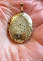 Front view of oval floral engraved locket in hand showing engraving details and bail